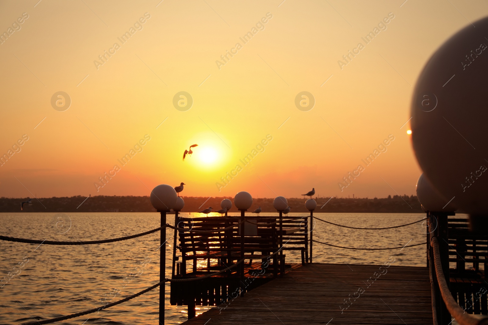 Photo of Picturesque view of empty wooden pier with lanterns at sunset