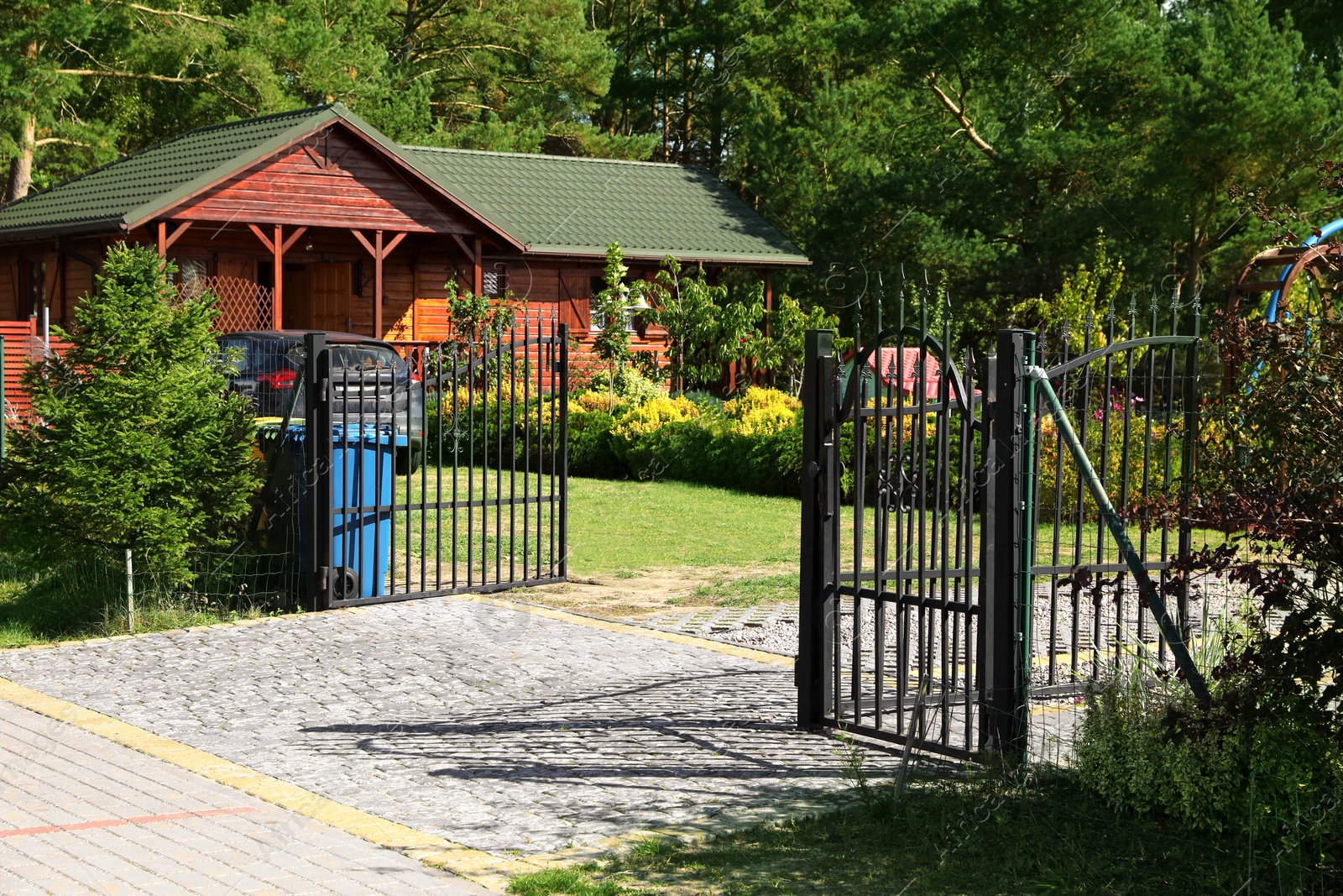 Photo of Open metal gates near house, trees and bushes outdoors