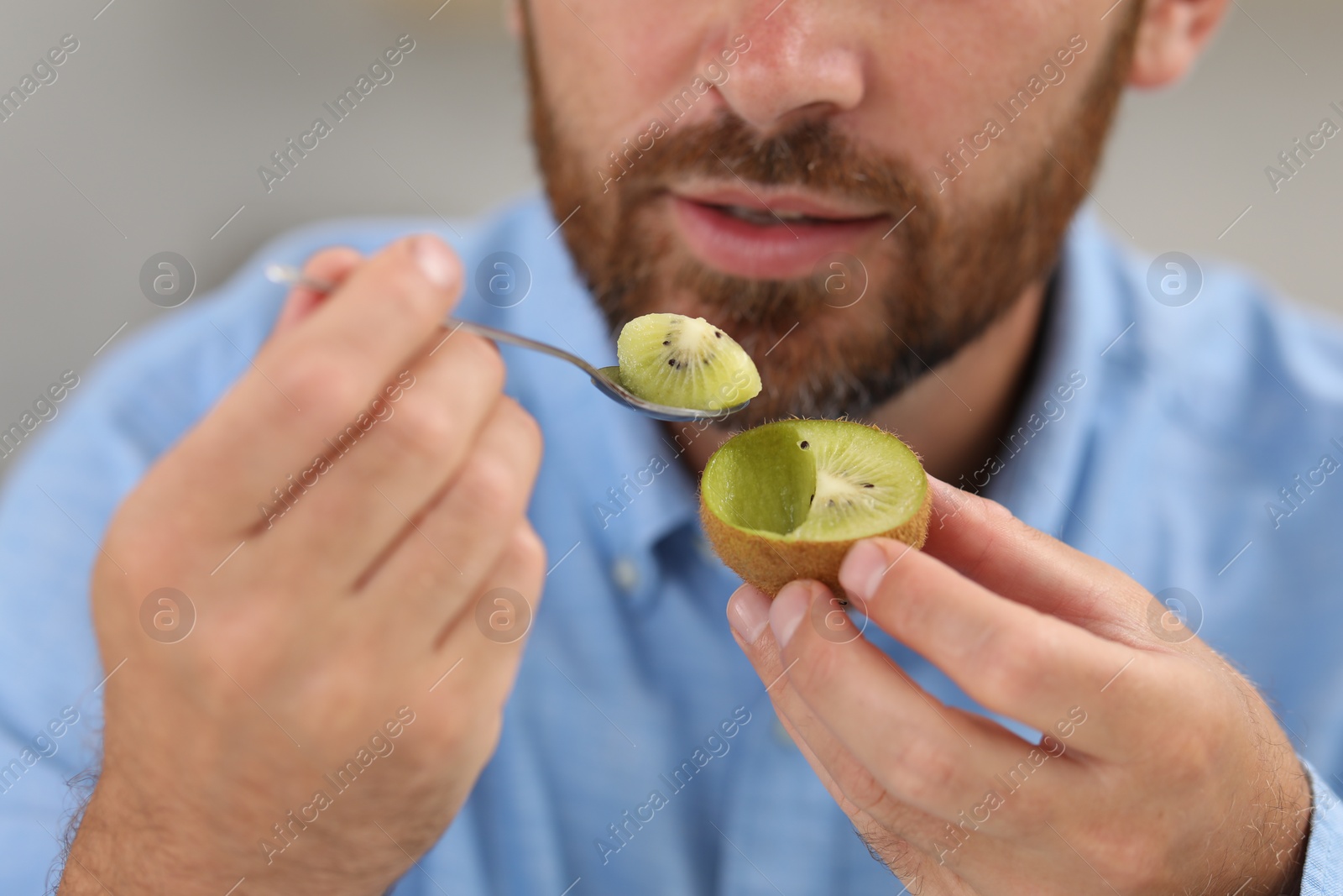 Photo of Man eating fresh kiwi with spoon, closeup