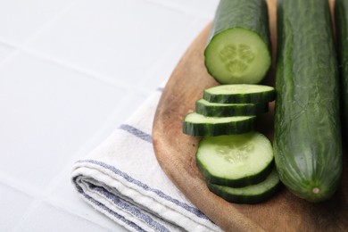 Photo of Fresh cucumbers on white tiled table, closeup. Space for text