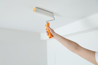 Photo of Worker painting ceiling with white dye indoors, closeup