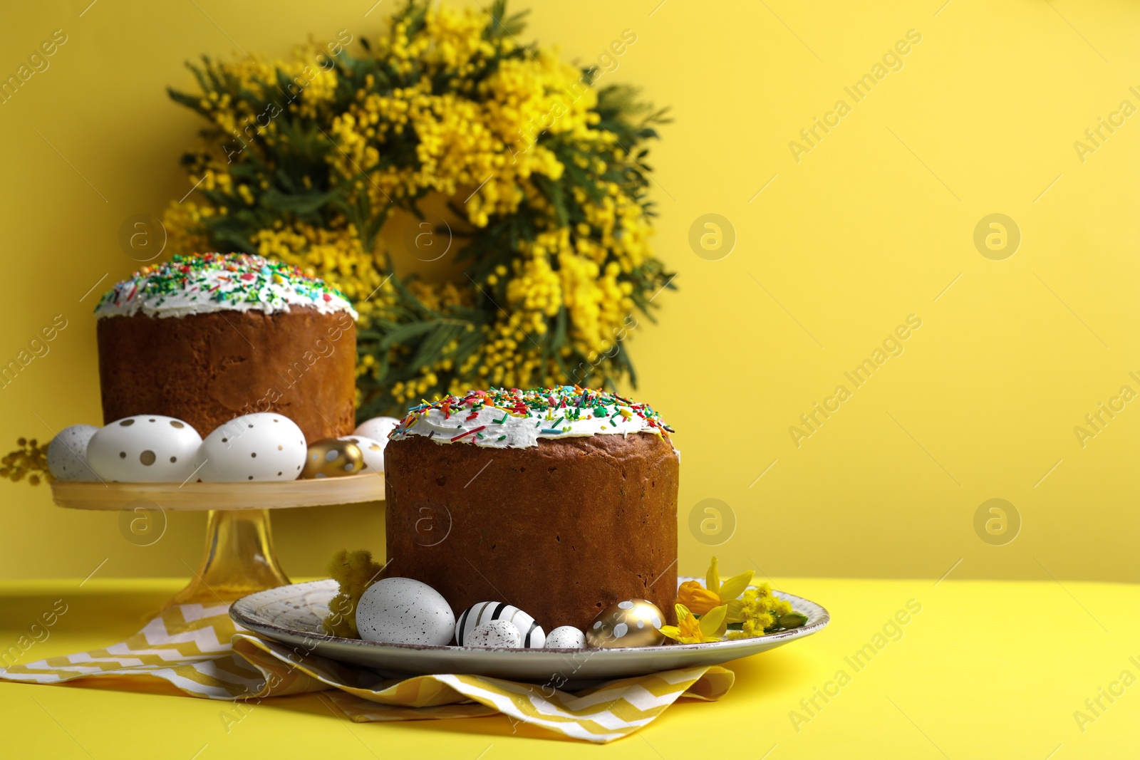 Photo of Traditional Easter cakes with sprinkles, painted eggs and beautiful spring flowers on yellow background