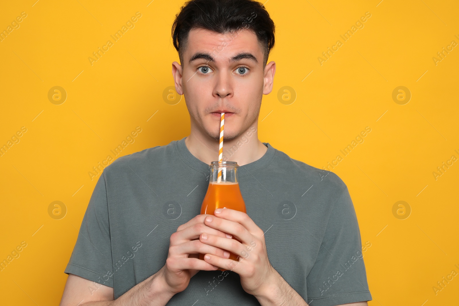 Photo of Handsome young man drinking juice on orange background