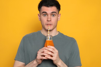 Handsome young man drinking juice on orange background