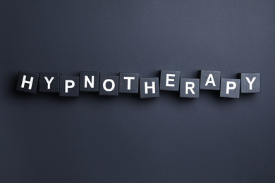 Photo of Wooden blocks with word HYPNOTHERAPY on black background, flat lay