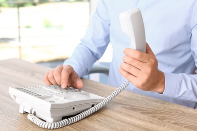 Photo of Man dialing number on telephone at workplace