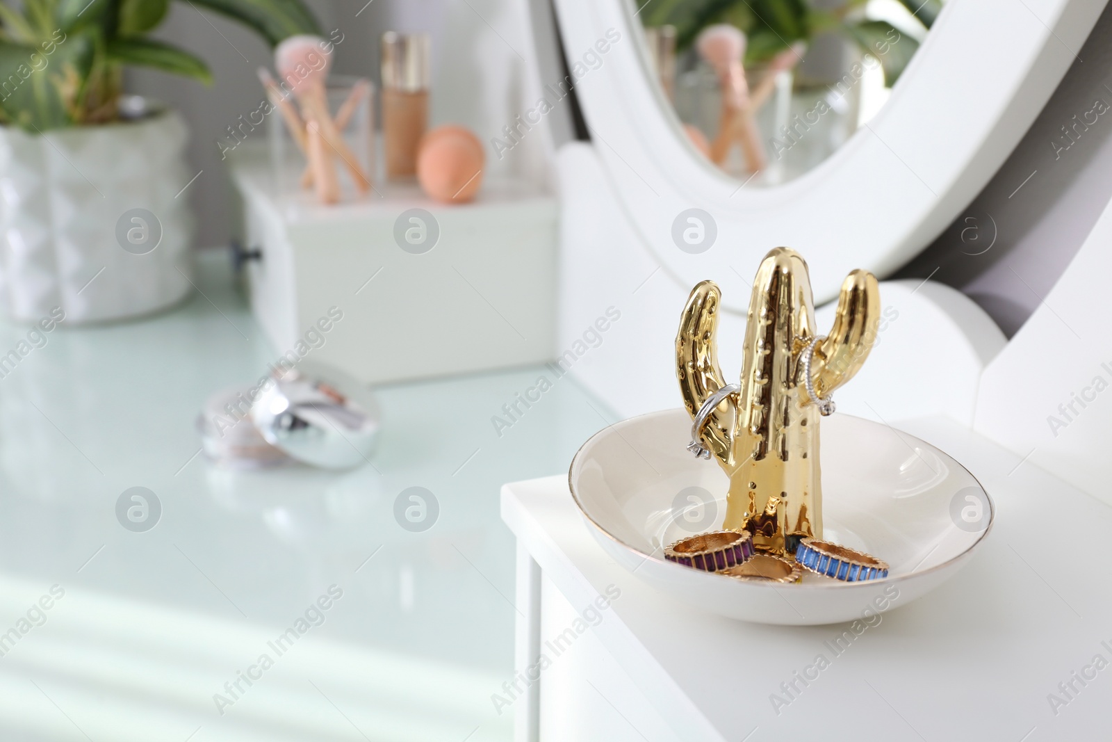 Photo of Cactus shape holder with stylish bijouterie on white dressing table, closeup. Space for text