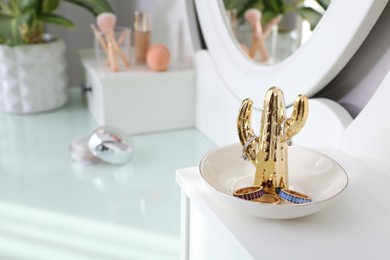Photo of Cactus shape holder with stylish bijouterie on white dressing table, closeup. Space for text