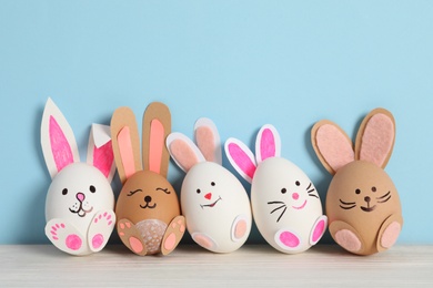 Photo of Eggs as cute bunnies on white wooden table against light blue background. Easter celebration