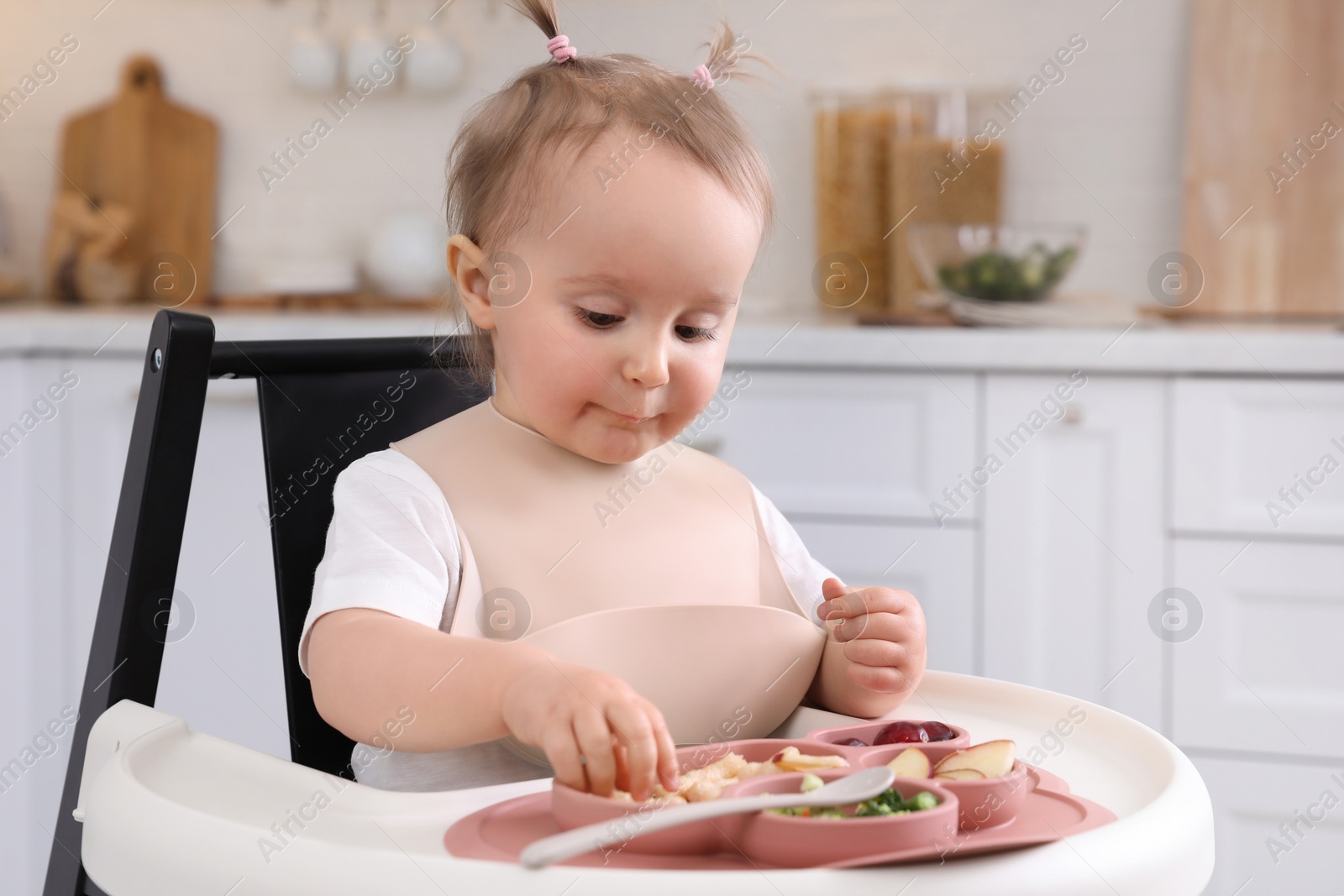 Photo of Cute little baby eating food in high chair at kitchen