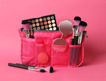 Cosmetic bag with makeup products and beauty accessories on pink background