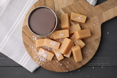 Photo of Yummy caramel candies and sea salt on wooden table, top view