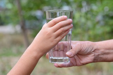 Child giving glass of water to elderly woman outdoors, closeup