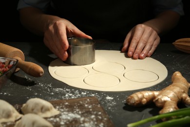 Woman cutting dough for gyoza at grey table, closeup