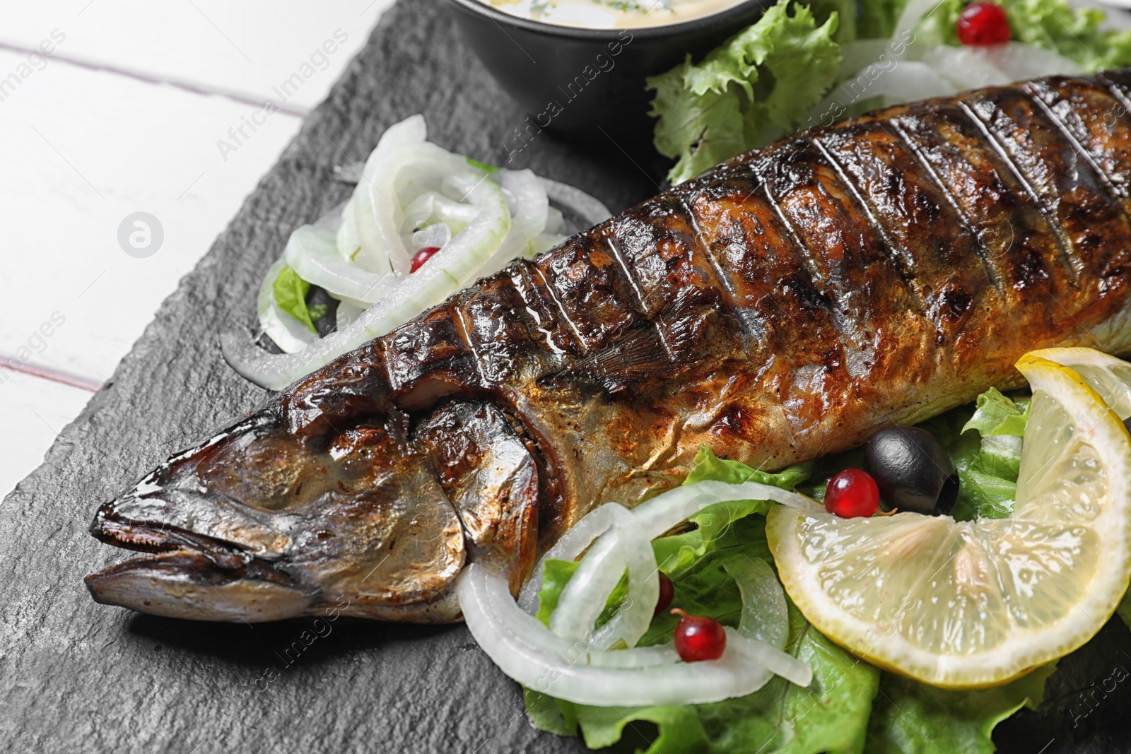 Photo of Slate plate with delicious grilled fish and sauce on table, closeup