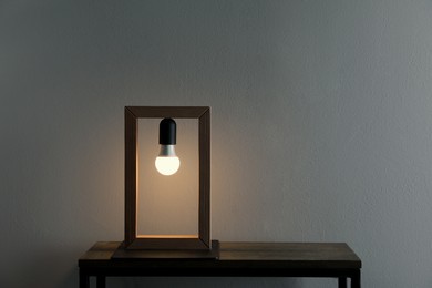 Photo of Wooden table with modern lamp near grey wall in room, space for text