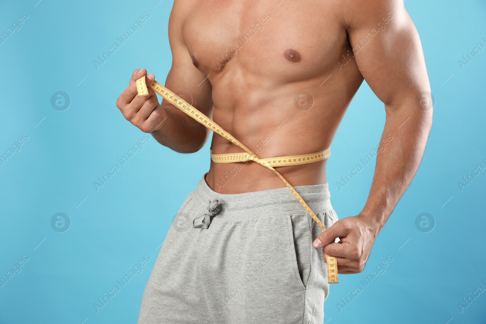 Photo of Young man with slim body using measuring tape on light blue background, closeup view