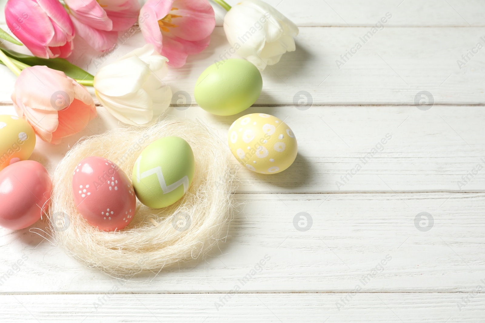 Photo of Composition with painted Easter eggs and flowers on wooden background, above view. Space for text
