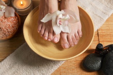 Photo of Woman soaking her feet in bowl with water and flower, closeup. Pedicure procedure