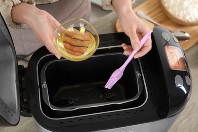 Woman spreading breadmaker pan with oil at table, above view