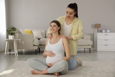 Doula massaging pregnant woman in living room. Preparation for child birth