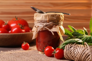 Photo of Jar of tasty tomato paste with spoon, ingredients and thread on table