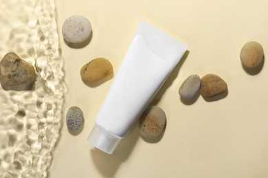 Tube of face cleansing product and stones in water against beige background, flat lay