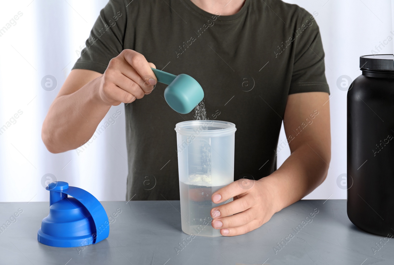 Photo of Man preparing protein shake with powder at table, closeup