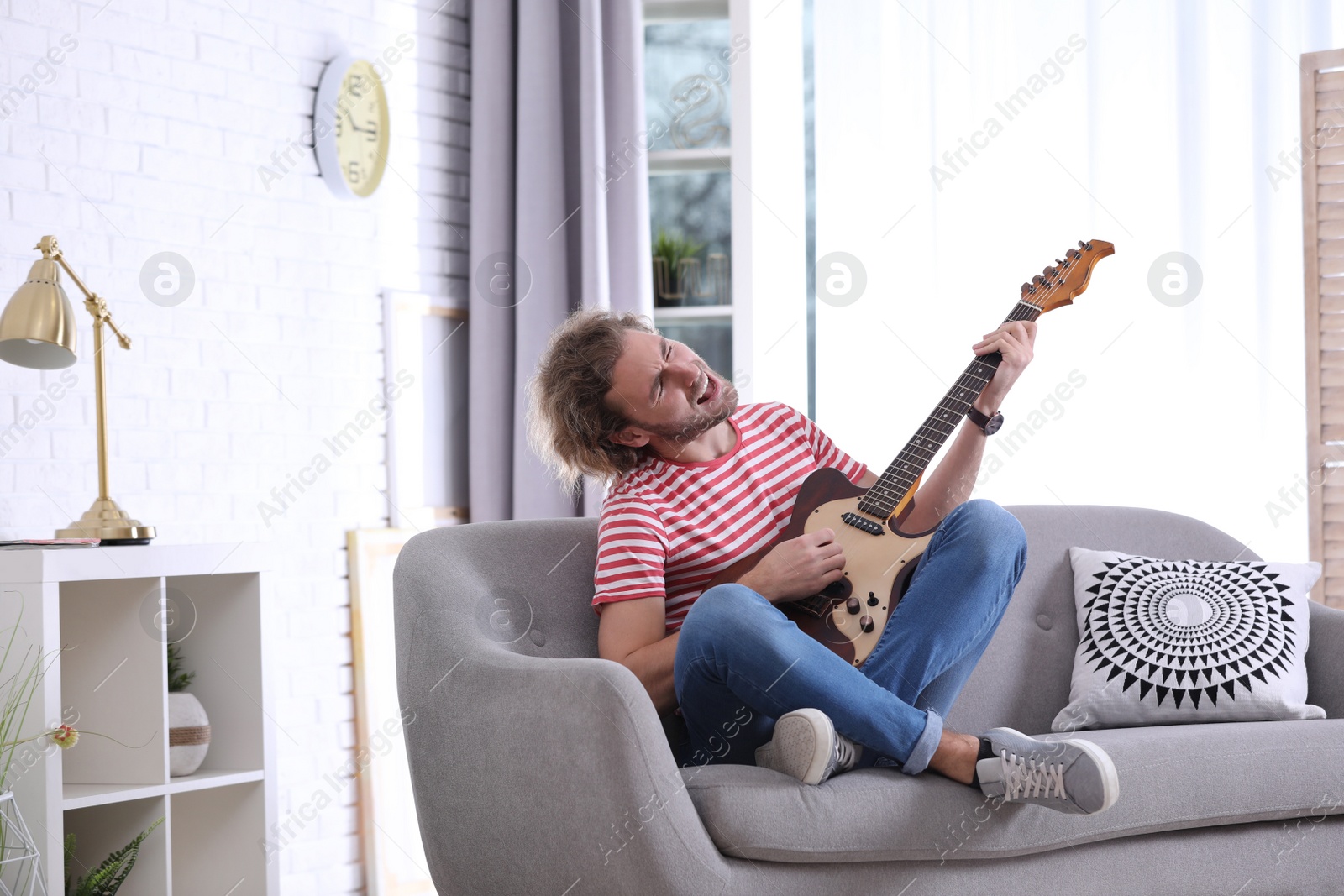 Photo of Young man playing electric guitar in living room. Space for text