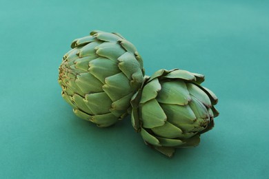 Photo of Whole fresh raw artichokes on green background, closeup