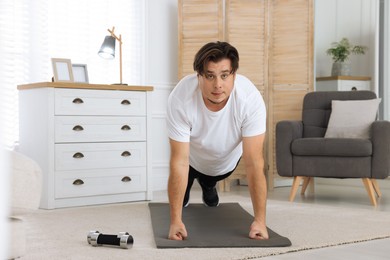 Photo of Overweight man doing plank exercise on mat at home