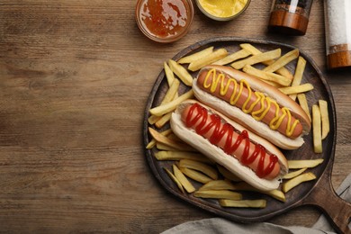 Photo of Delicious hot dogs with mustard, ketchup and potato fries on wooden table, flat lay. Space for text