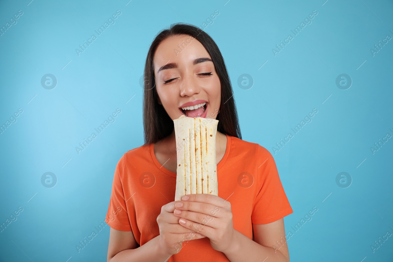 Photo of Young woman eating tasty shawarma on turquoise background