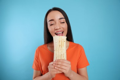 Young woman eating tasty shawarma on turquoise background