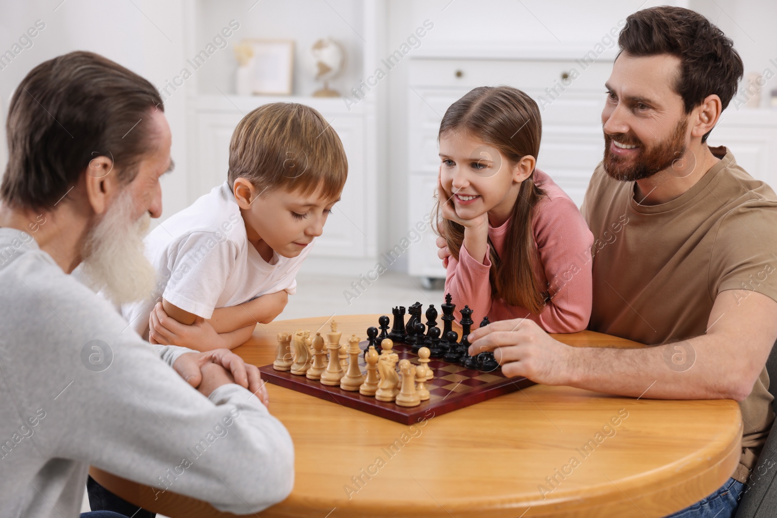 Photo of Family playing chess together at table in room