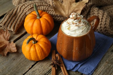 Mug of pumpkin spice latte with whipped cream and ingredients on wooden table