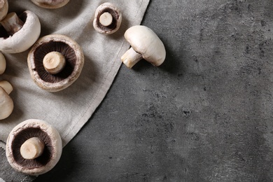 Photo of Fresh champignon mushrooms and napkin on grey background, top view with space for text