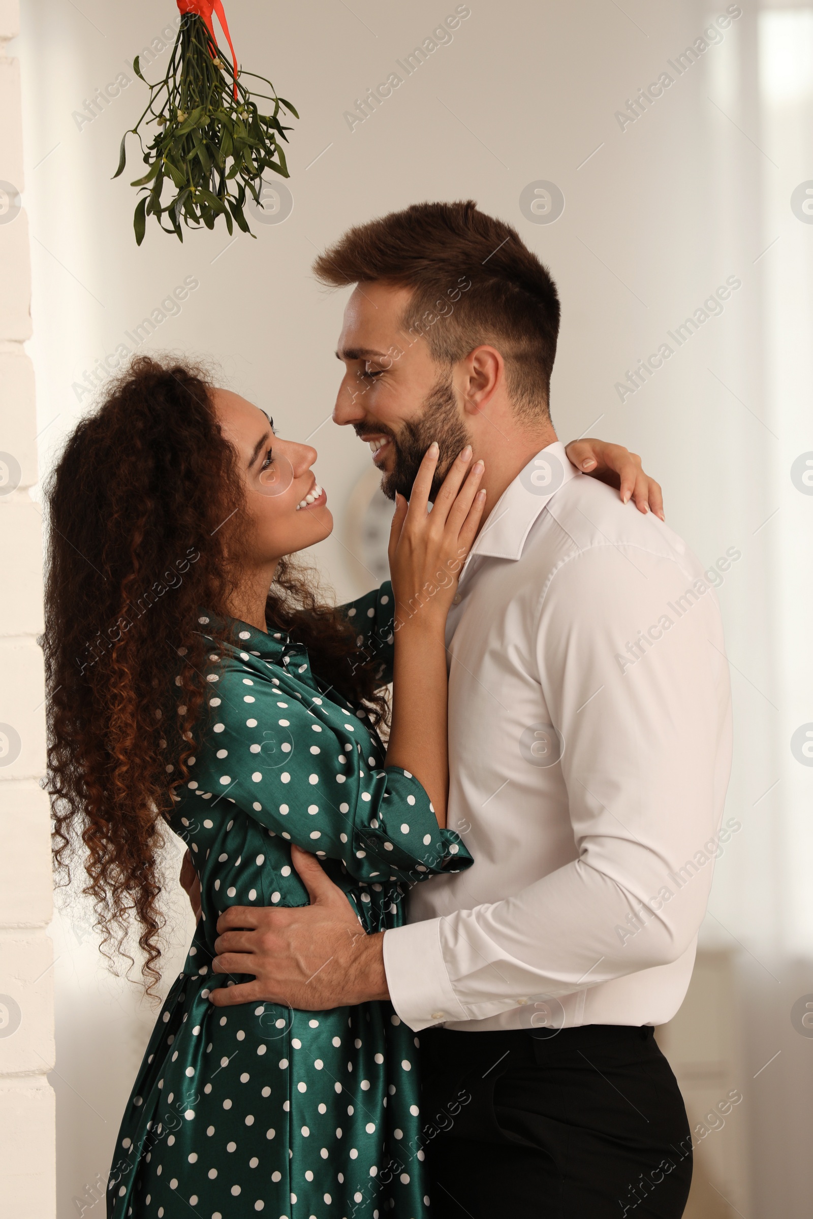 Photo of Lovely couple under mistletoe bunch in room. Christmas time