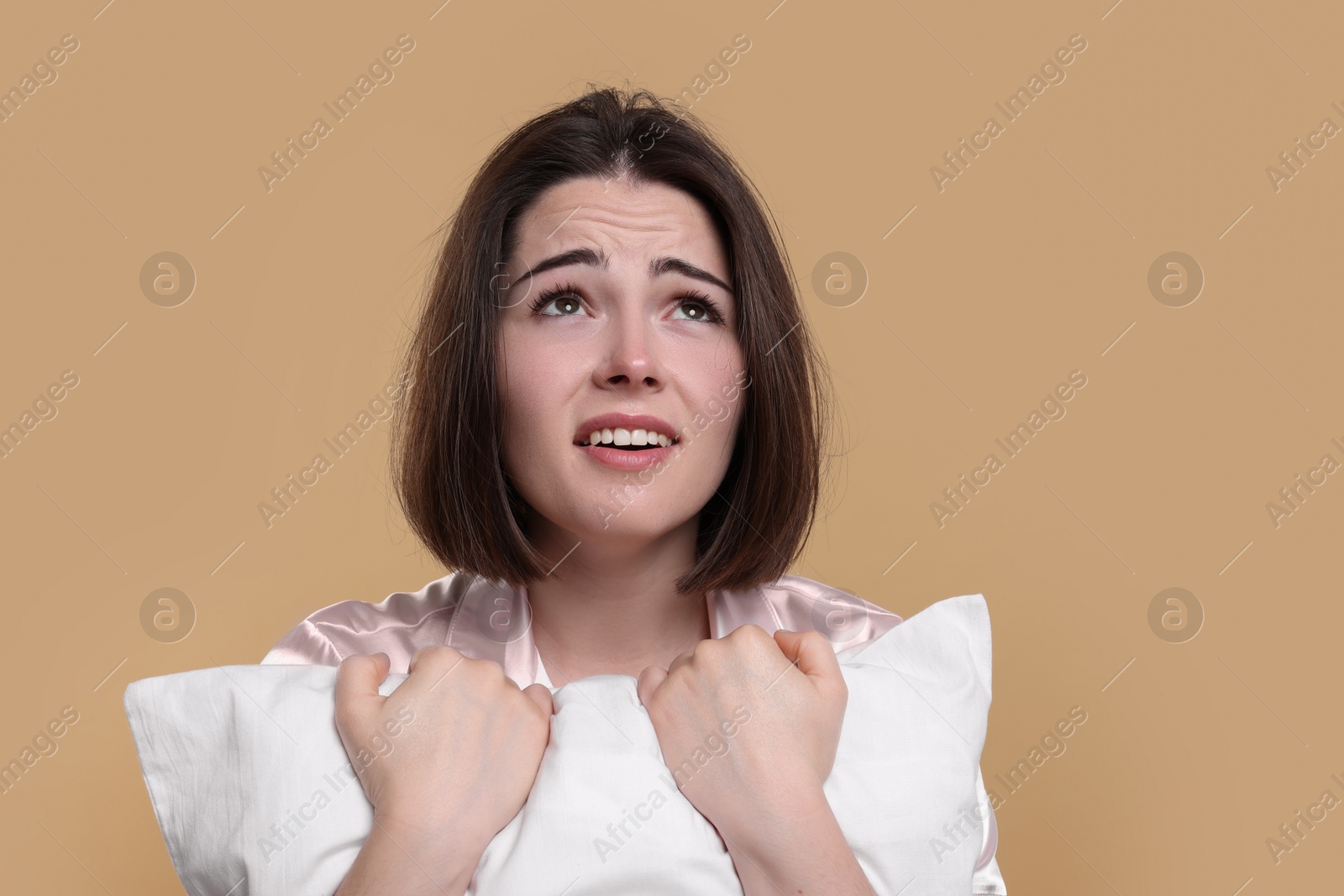 Photo of Unhappy young woman with pillow on beige background. Insomnia problem