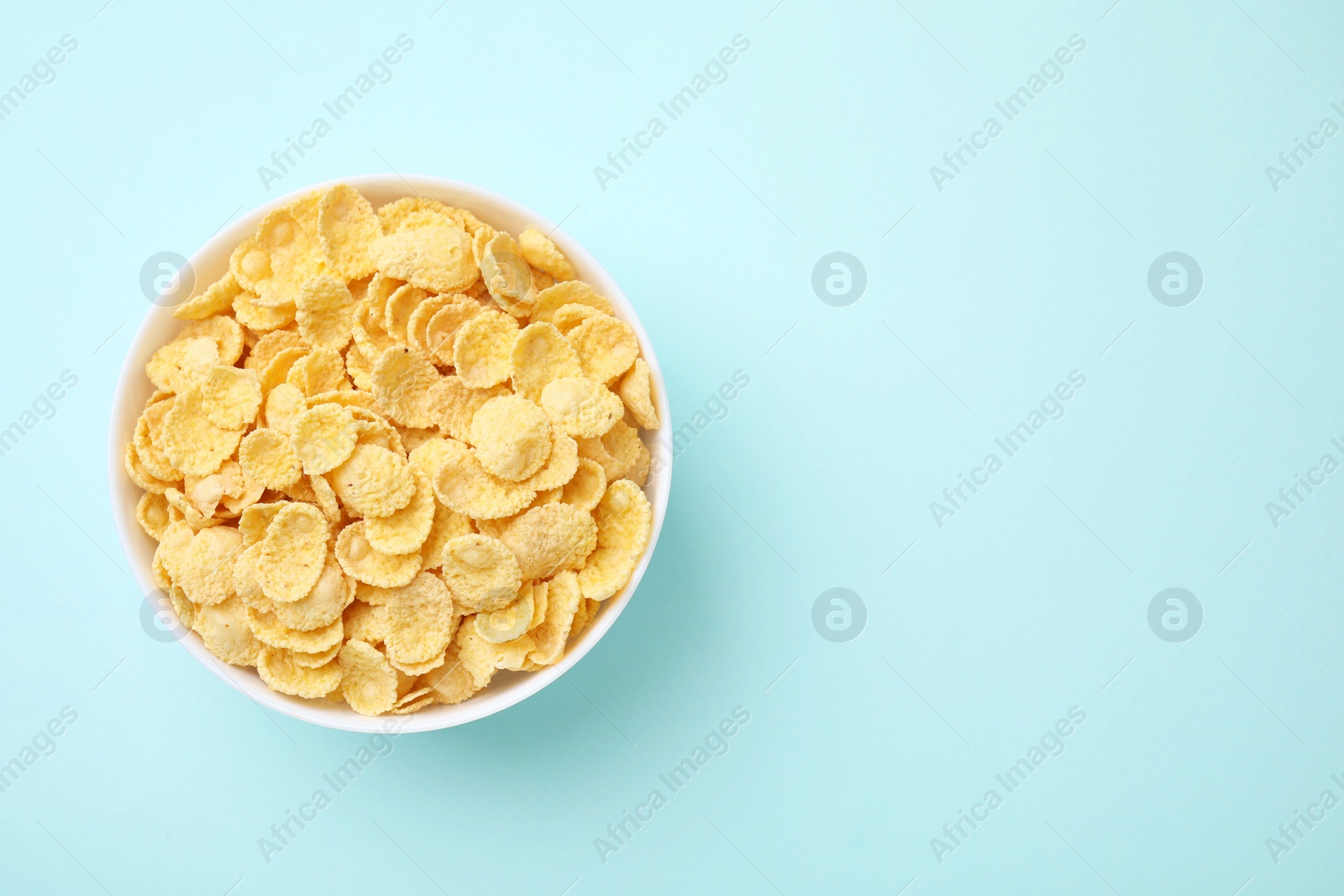 Photo of Breakfast cereal. Tasty corn flakes in bowl on light blue table, top view. Space for text