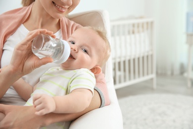 Lovely mother giving her baby drink from bottle in room. Space for text