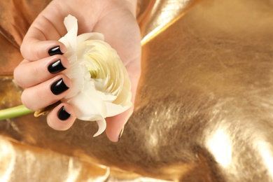 Photo of Woman with black manicure holding flower on golden background, closeup. Nail polish trends