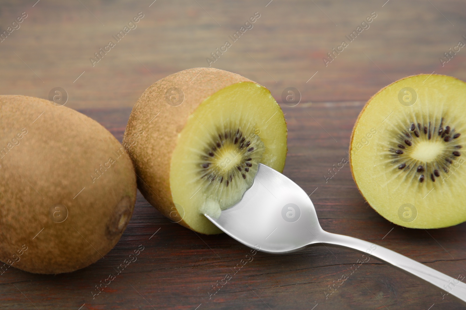 Photo of Fresh ripe yellow kiwis with spoon on wooden table