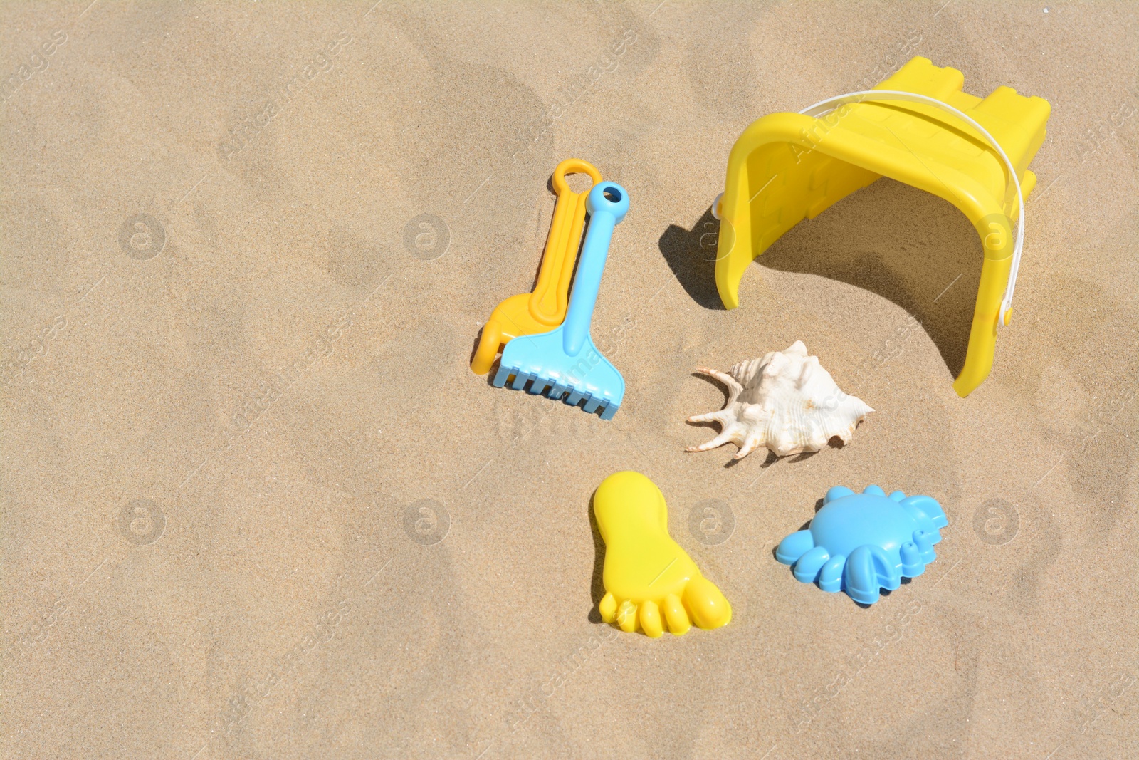 Photo of Bright plastic bucket and rakes on sand. Beach toys. Space for text