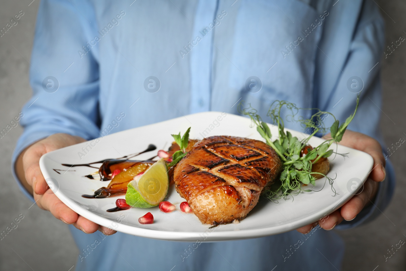 Photo of Woman holding plate with grilled duck breast on grey background, closeup