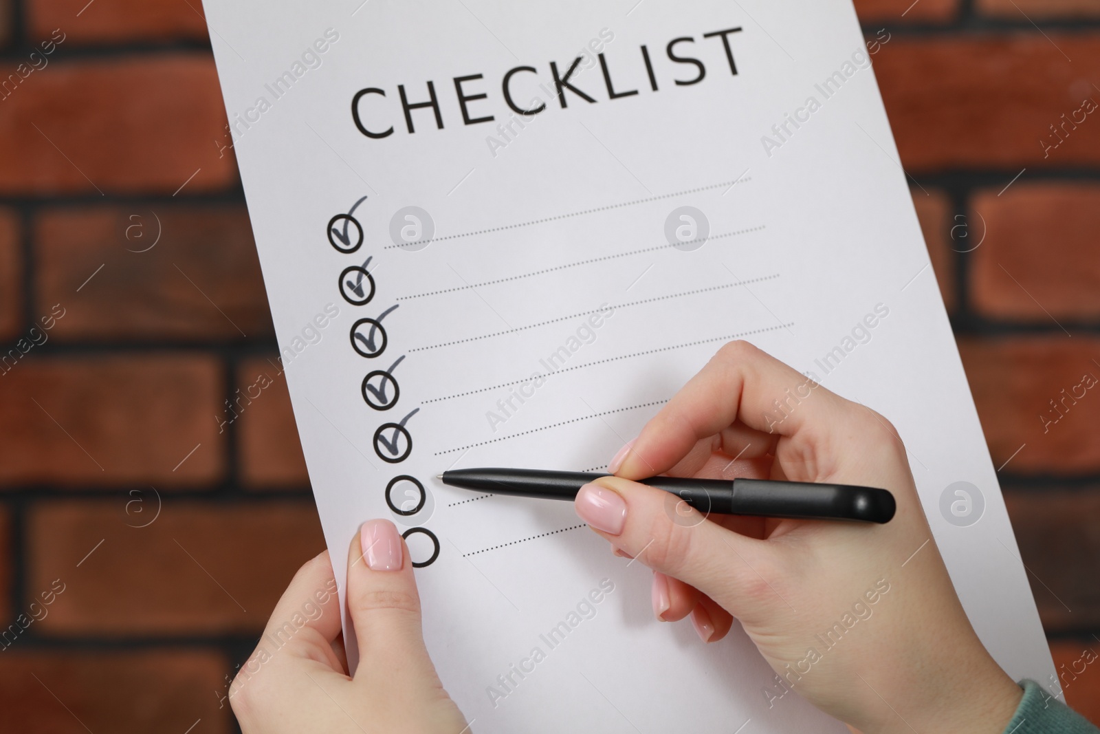 Photo of Woman filling Checklist against brick wall, closeup