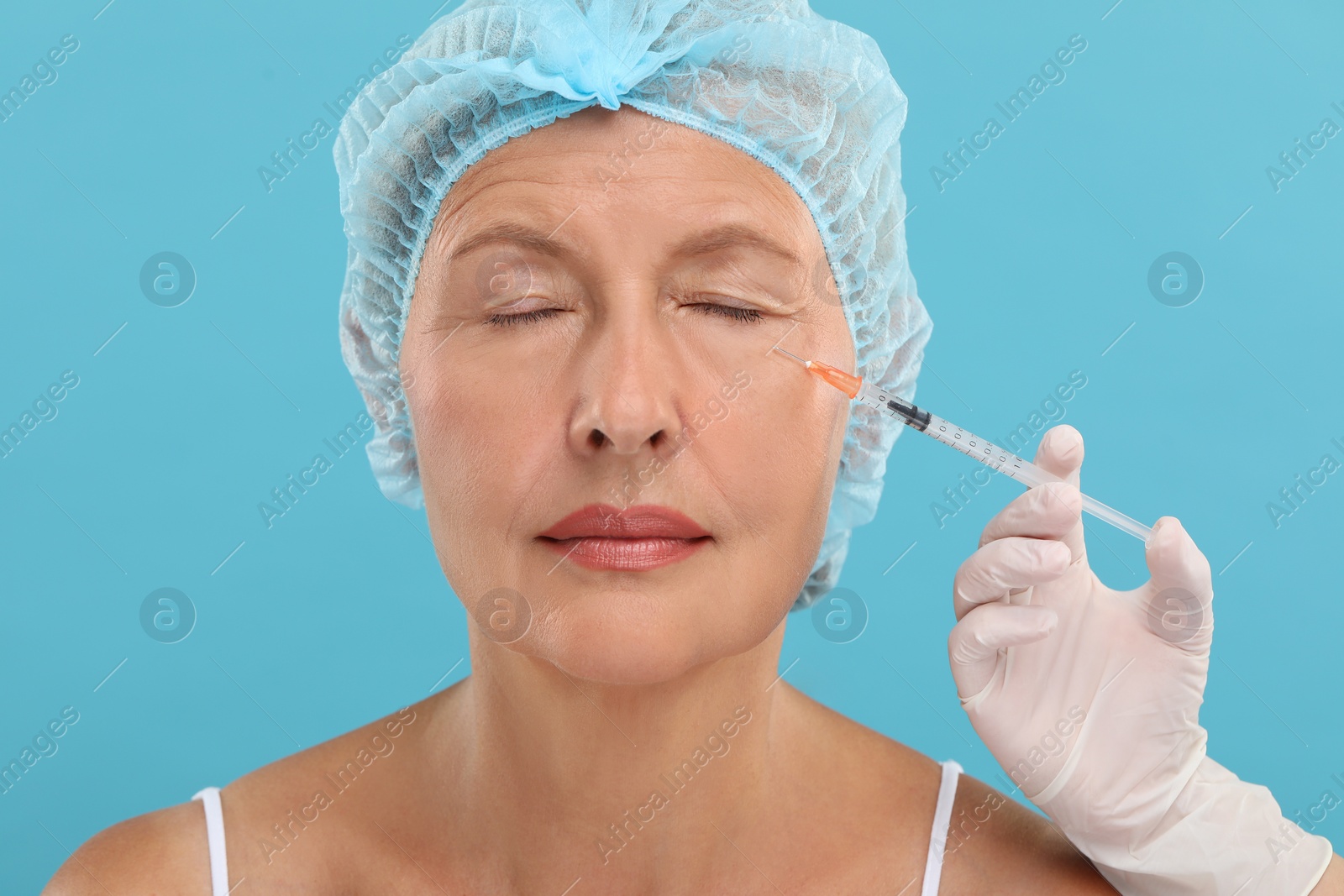 Photo of Doctor giving facial injection to senior woman on light blue background. Cosmetic surgery