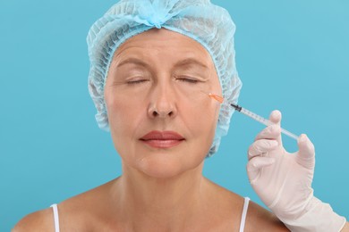 Photo of Doctor giving facial injection to senior woman on light blue background. Cosmetic surgery
