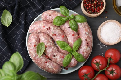 Photo of Raw homemade sausages, basil leaves, tomatoes and spices on grey wooden table, flat lay