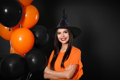 Photo of Beautiful woman wearing witch costume with balloons for Halloween party on black background